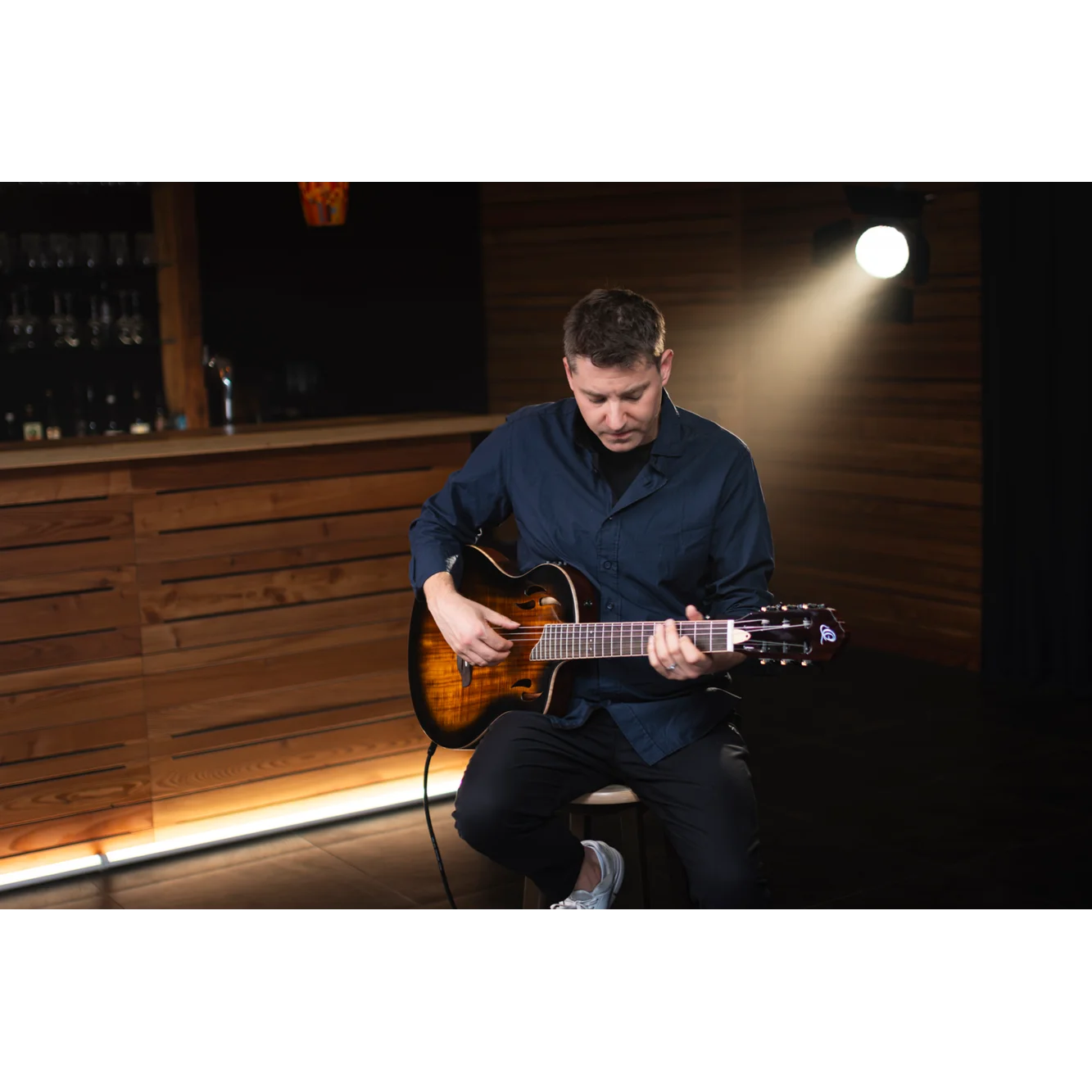 Man playing electric nylon string guitar in a dimly lit room with wooden walls in sydney, australia.