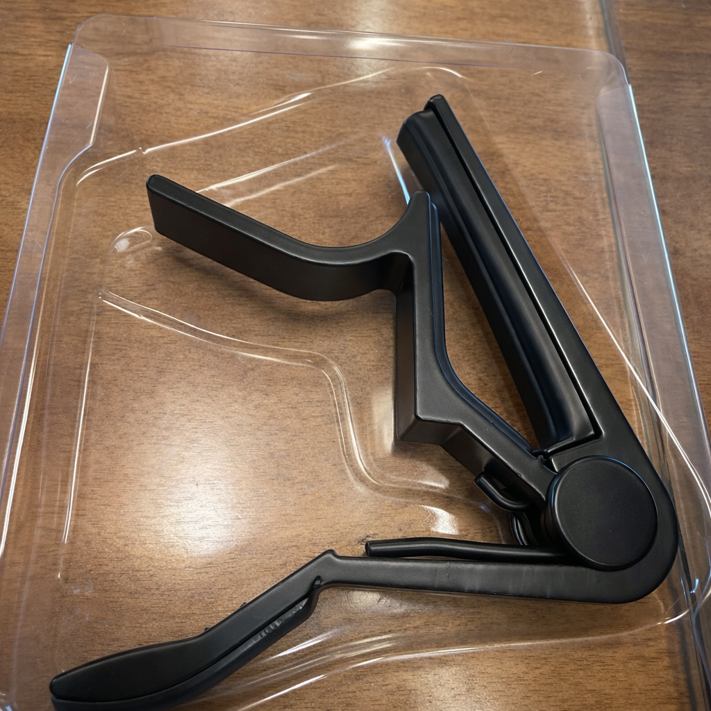 Black guitar capo on a clear plastic stand against a wooden background