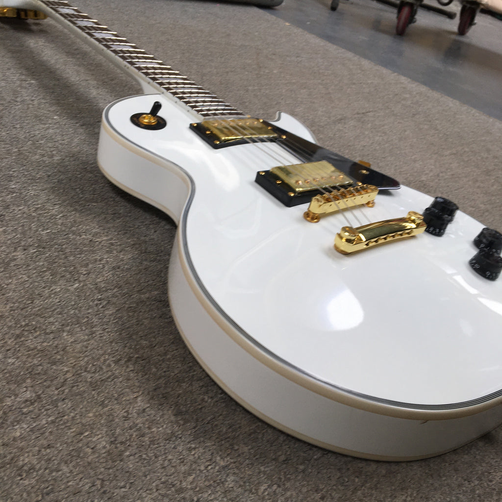 White electric guitar with gold hardware on a gray surface