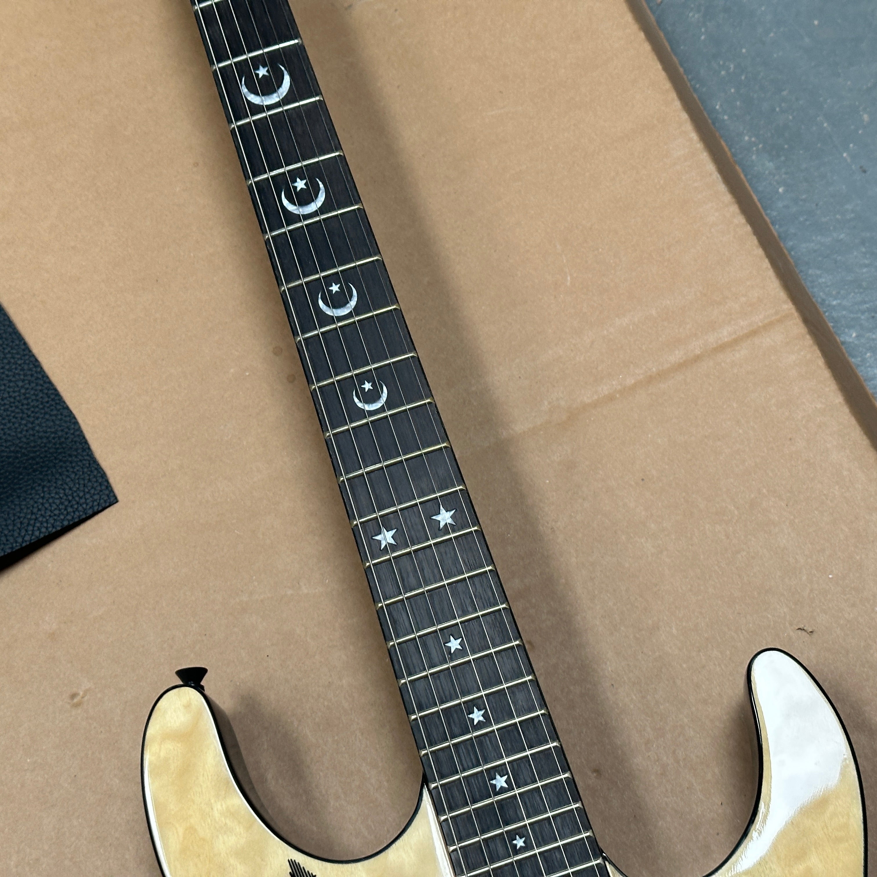 Close-up of a guitar neck with star and moon inlays on a brown surface. steel strings shown on the phot, the electric guitar is on sale in melbourne, sydney, brisbane , pretty much all over Australia.