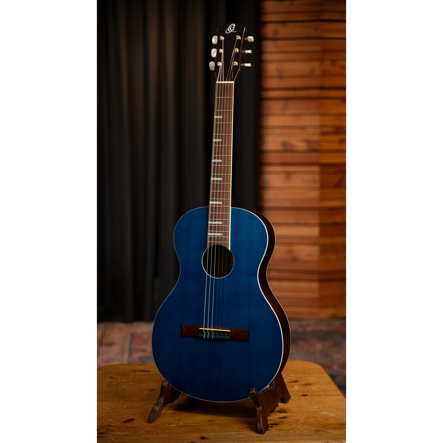 Blue acoustic guitar on a stand with a wooden background