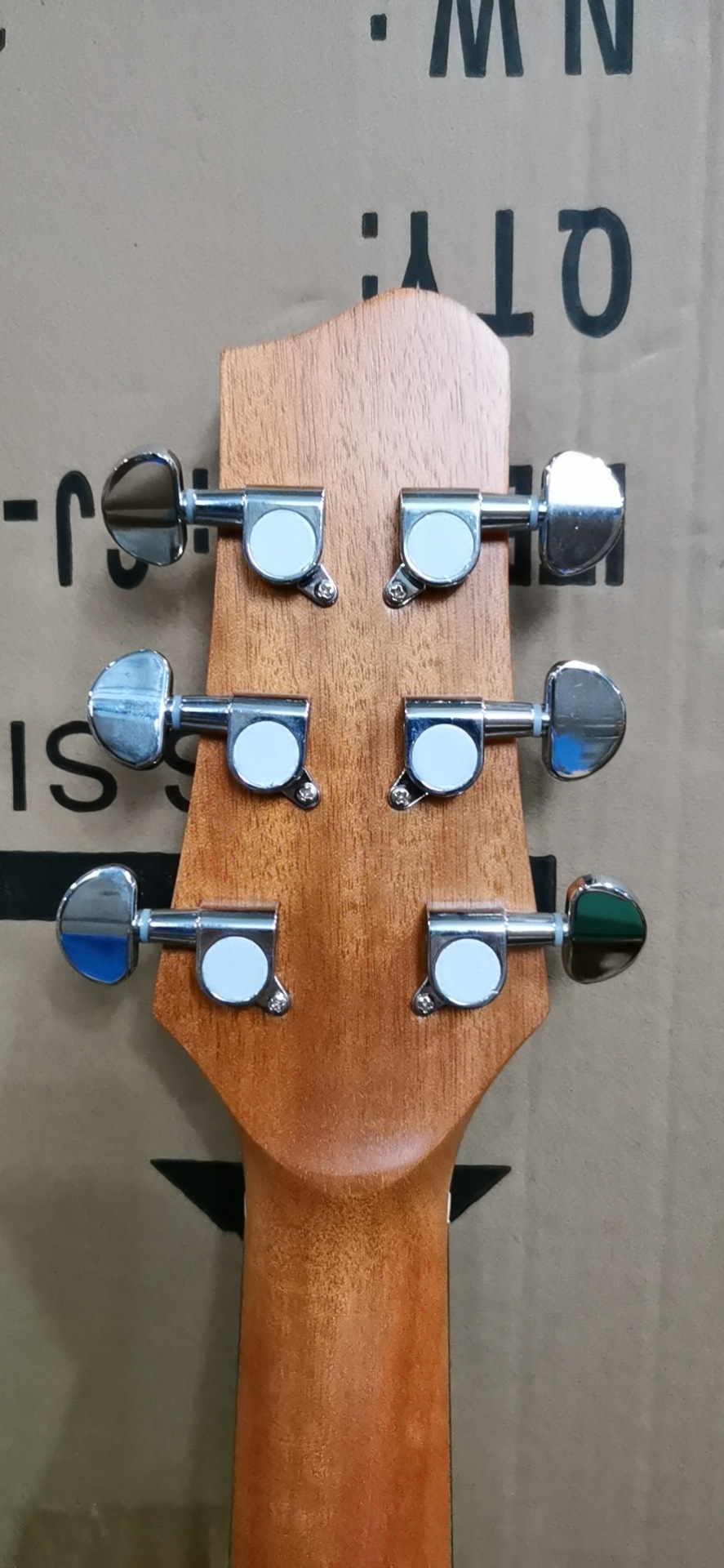 Close-up of a guitar headstock with tuning pegs against a cardboard background