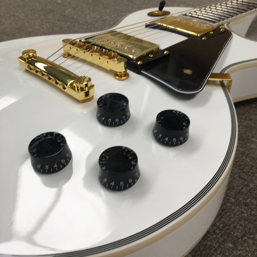 Close-up of a white electric guitar with gold hardware and black control knobs.