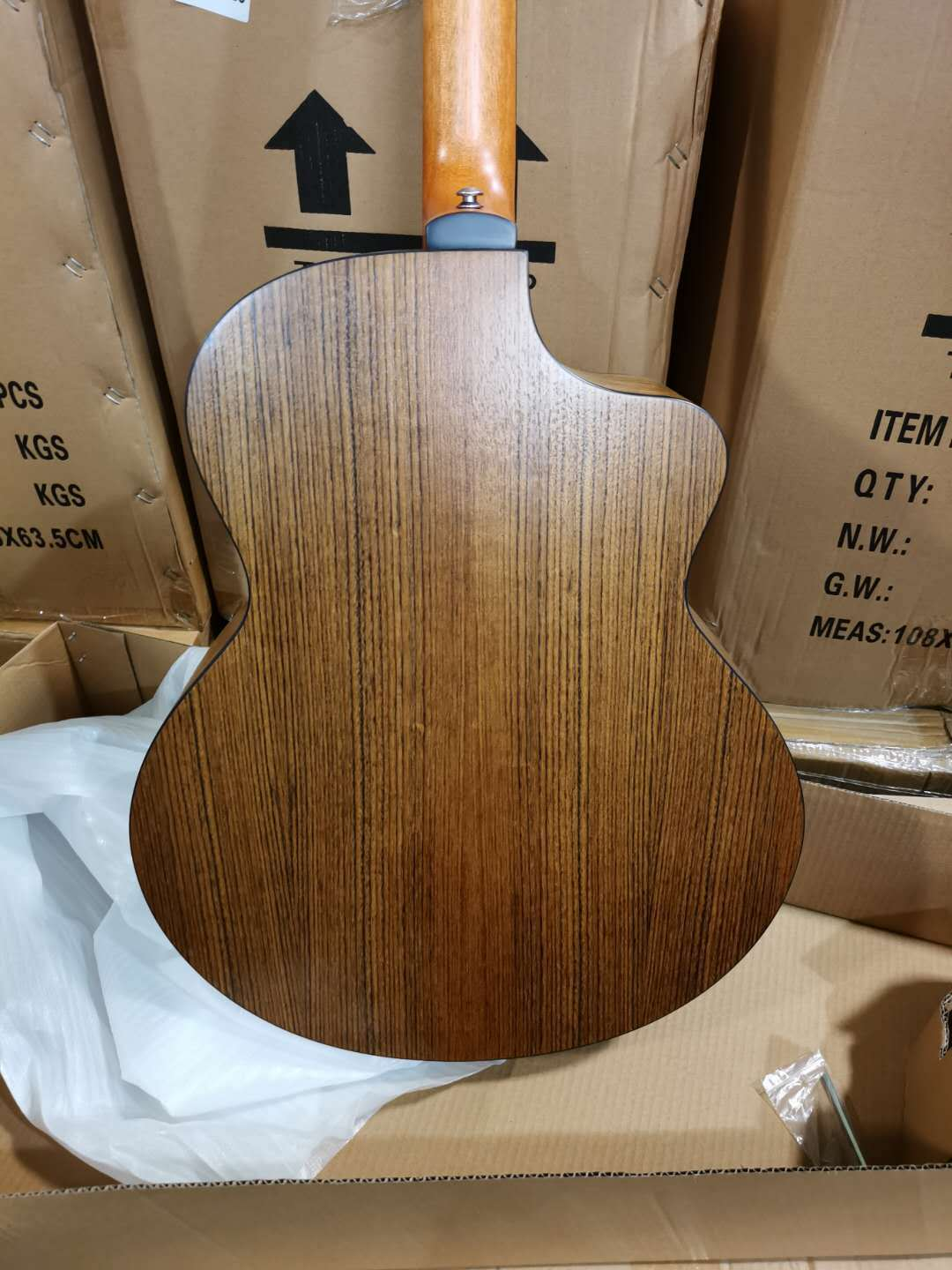 Back view of a wooden acoustic guitar in an open cardboard box