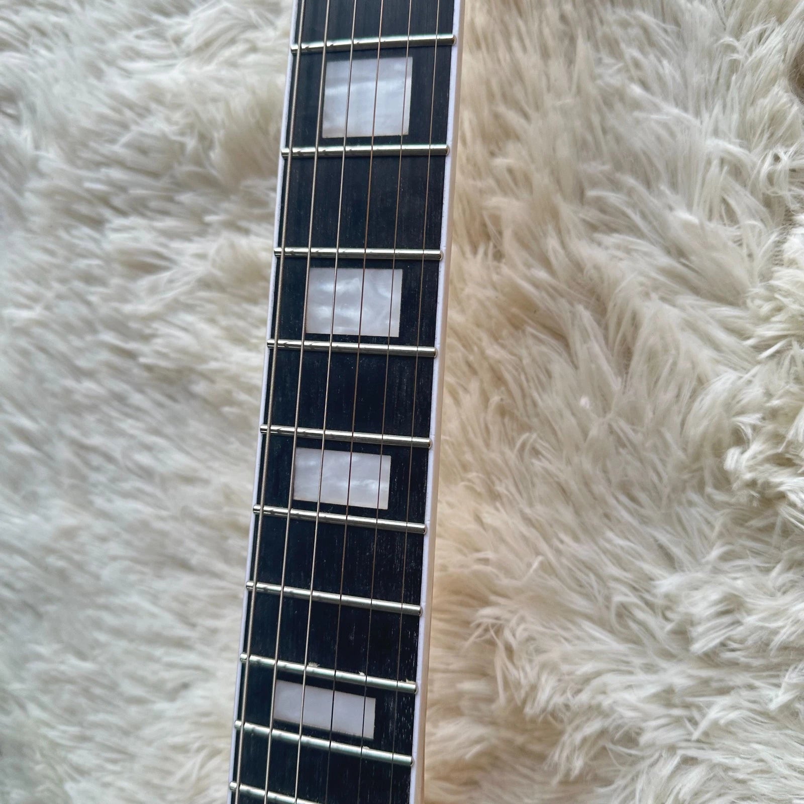 Guitar neck with fret markers on a fluffy white surface, shows all the 6 steel strings thats on sale in Melbourne, Brisbane australia.