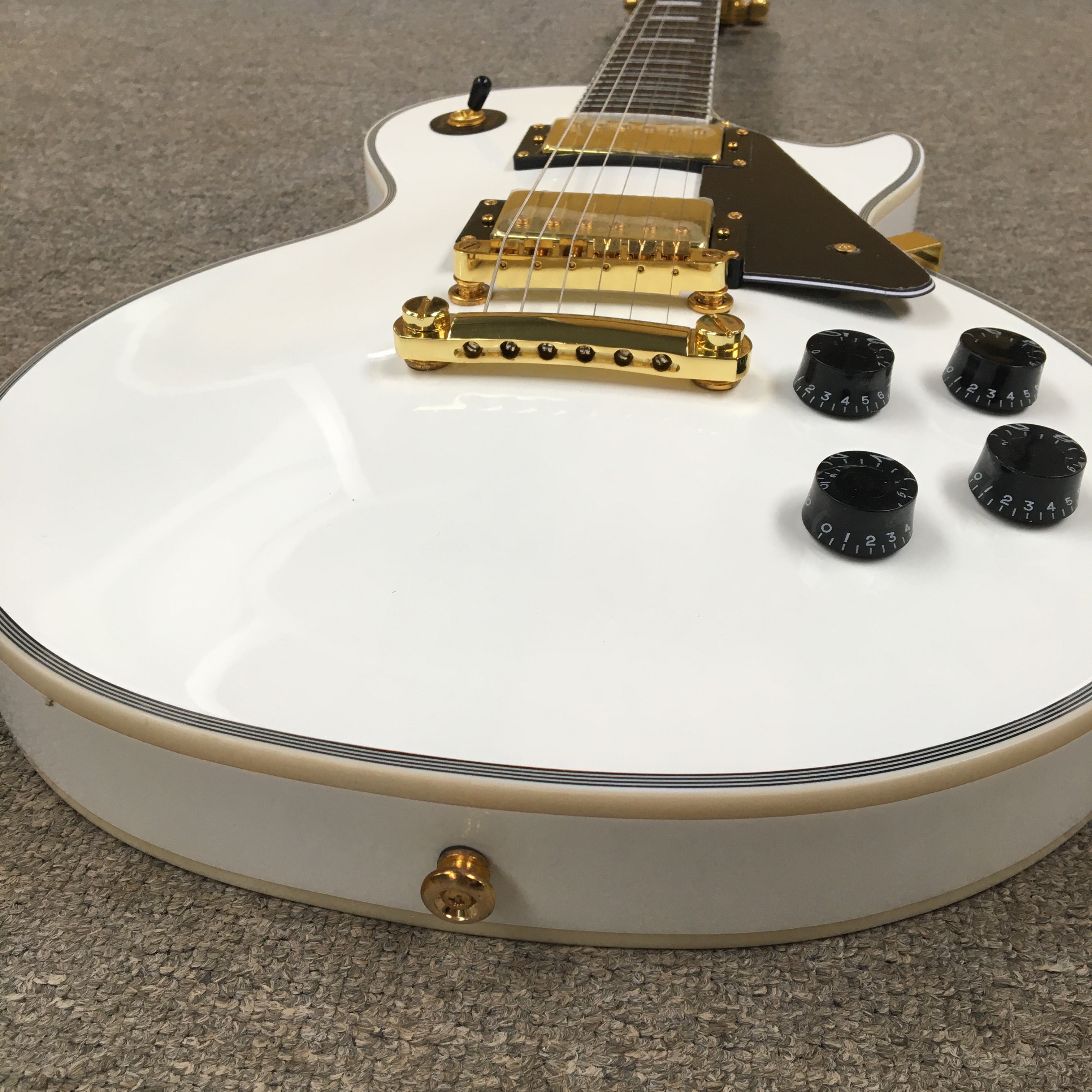 White electric guitar with gold hardware on a gray surface