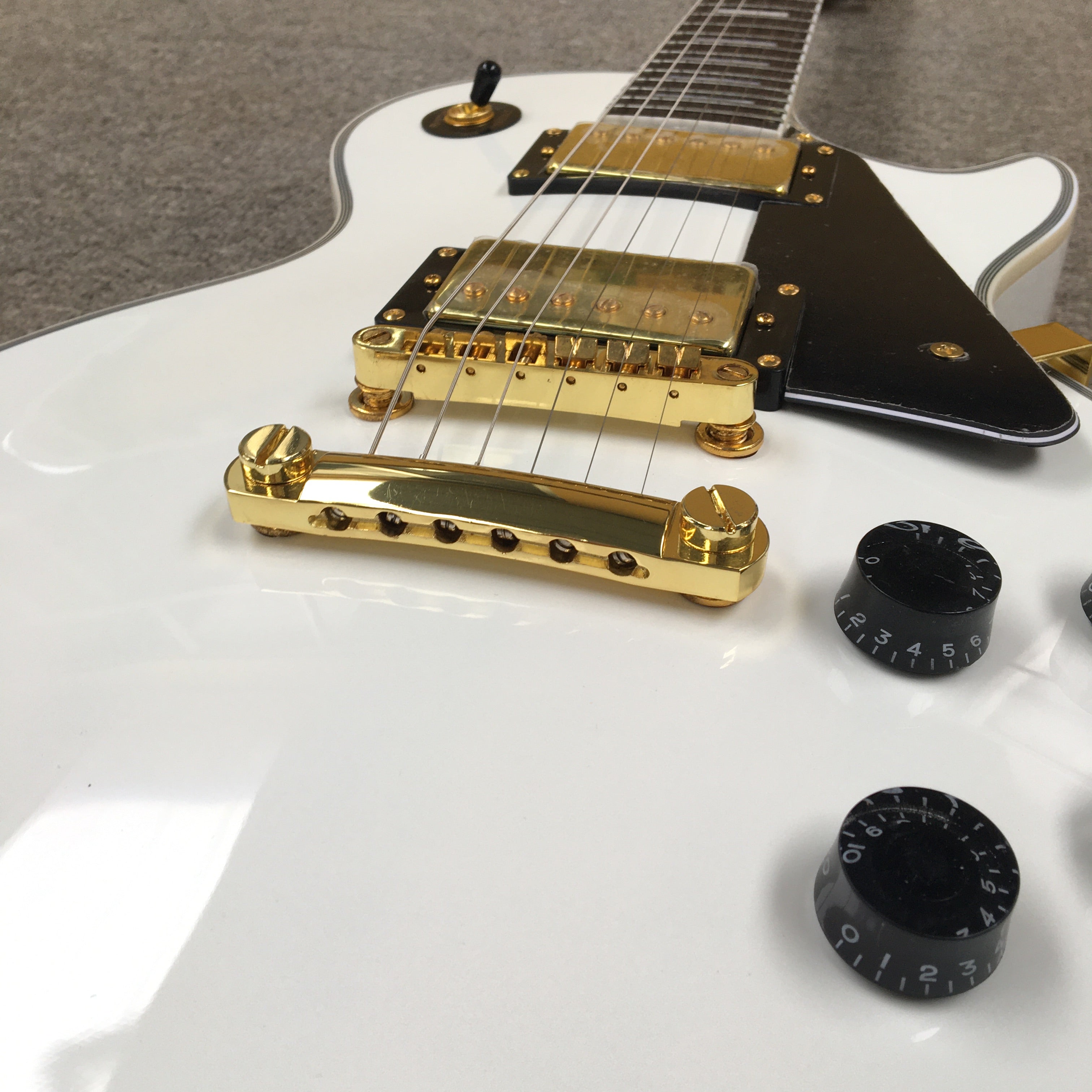 Close-up of a white electric guitar with gold hardware on a gray surface